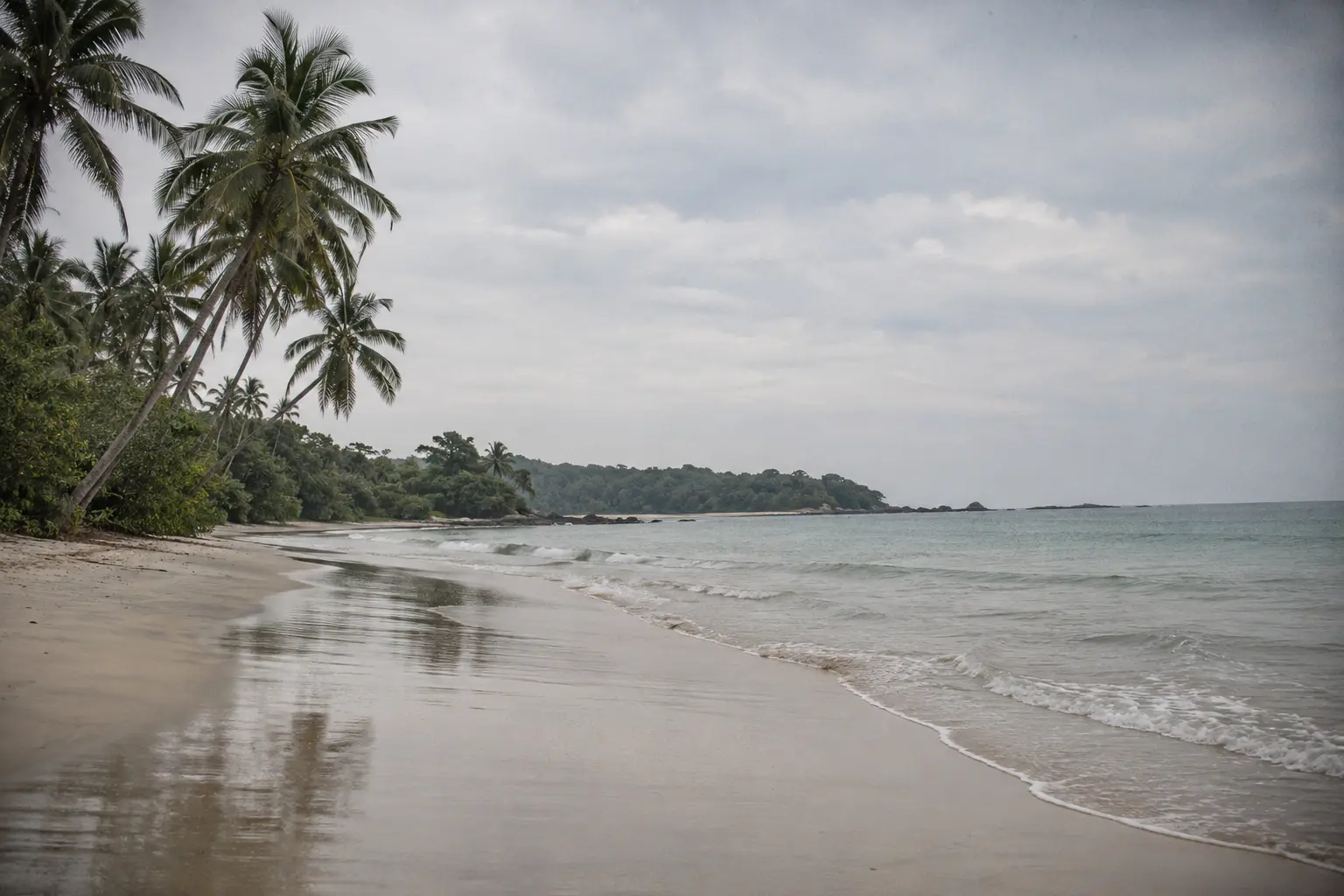Empty beach near Trincomalee with wet sand reflecting a pale sky